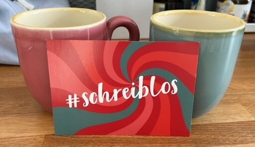 Bunte Postkarte von Treffpunktschreiben vor zwei großen Teetassen. Auf der Postkarte steht #schreiblos